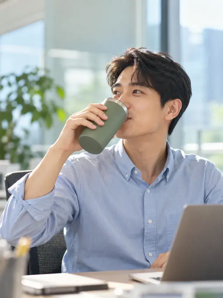 사무실 책상에서 개인 텀블러로 음료를 마시는 직장인